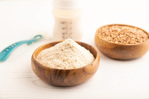 Powdered milk and buckwheat baby food mix, infant formula, pacifier, bottle, spoon on white wooden