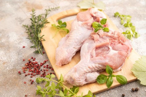 Raw turkey wing with herbs and spices on a wooden cutting board on a brown concrete background.