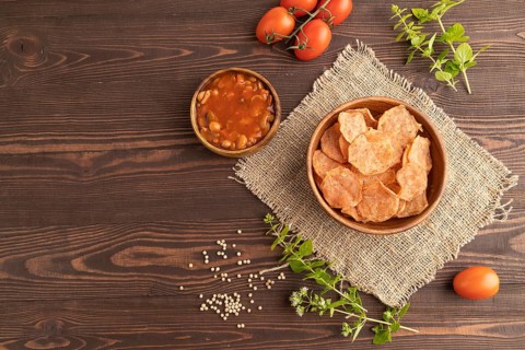Slices of dehydrated salted meat chips with herbs and spices on brown wooden background and linen