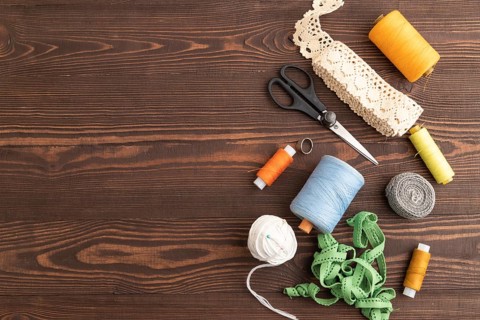 Sewing accessories: scissors, thread, thimbles, braid on brown wooden background. Top view, flat
