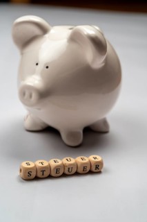 White piggy bank and tax lettering against a white background, studio photo, Germany, Europe