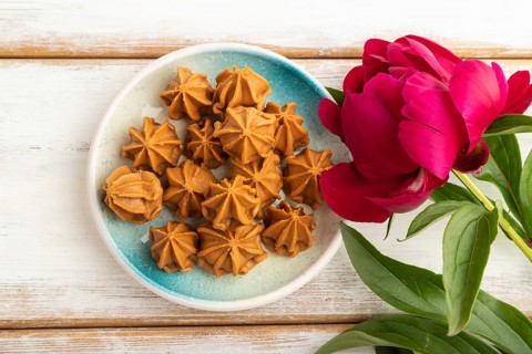 Homemade soft caramel fudge candies on blue plate on white wooden background, peony flower