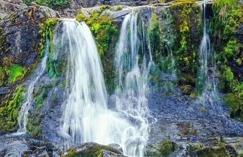 Small picturesque waterfall, white water falling over moss-covered rocks, motion blur, long