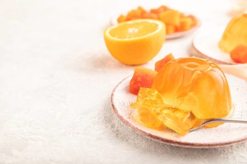 Papaya and orange jelly on gray concrete background and orange linen textile. side view, flat lay,
