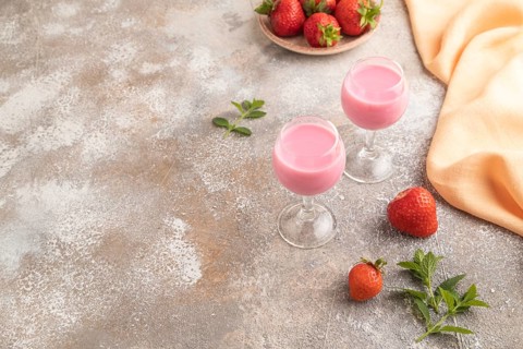 Sweet strawberry liqueur in glass on a gray concrete background and orange textile. side view, copy
