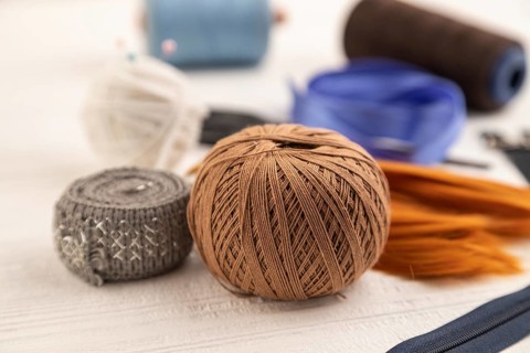 Sewing accessories: scissors, thread, thimbles, braid on white wooden background. Side view, close
