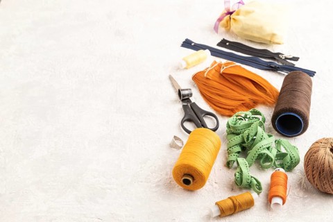 Sewing accessories: scissors, thread, thimbles, braid on gray concrete background. Side view, copy