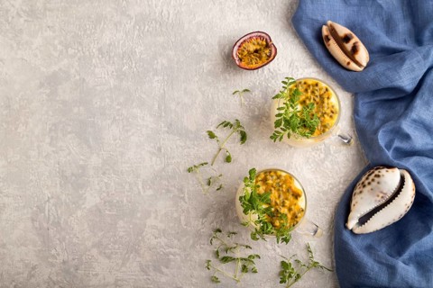 Yogurt with passionfruit and marigold microgreen in glass on gray concrete background with blue