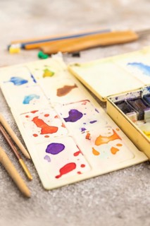 Drawing accessories set: brushes, pencils, watercolor on brown concrete background. Side view,