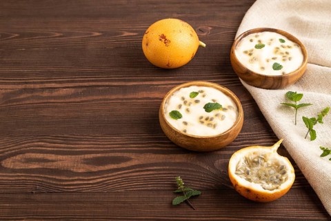 Yoghurt with granadilla and mint in wooden bowl on brown wooden background and linen textile. side