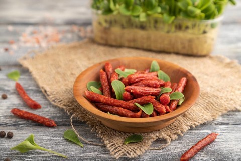 Small smoked sausage with borage microgreen, salt and pepper on gray wooden background and linen