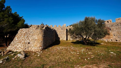Part of the fortress wall surrounded by trees and grass, Chlemoutsi, High Medieval Crusader castle,
