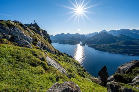 Mountaineer on the summit of Dronningsvarden or Stortinden, behind sea and fjord Umvagsundet,