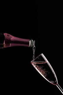 Pink champagne is poured into a slanted glass against a black background
