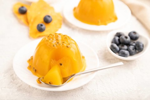 Mango and passion fruit jelly with blueberry on gray concrete background and linen textile. side