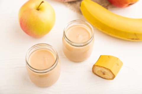 Baby puree with fruits mix, apple, banana infant formula in glass jar on white wooden background.