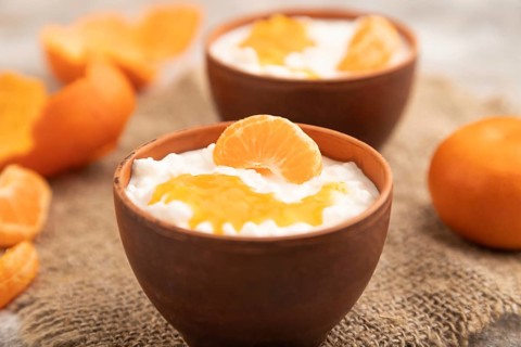 Grained cottage cheese with tangerine jam on brown concrete background and linen textile. side