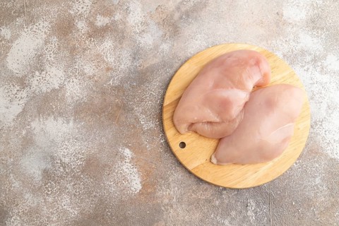 Raw chicken breast on a wooden cutting board on a brown concrete background. Top view, flat lay,