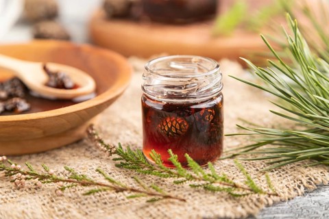 Pine cone jam with herbal tea on gray wooden background and linen textile. Side view, close up,