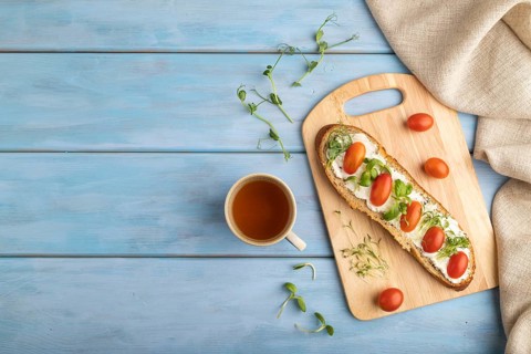 Long white bread sandwich with cream cheese, tomatoes and microgreen on blue wooden background and