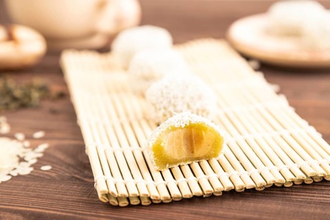 Japanese rice sweet buns mochi filled with pandan and coconut jam and cup of green tea on brown