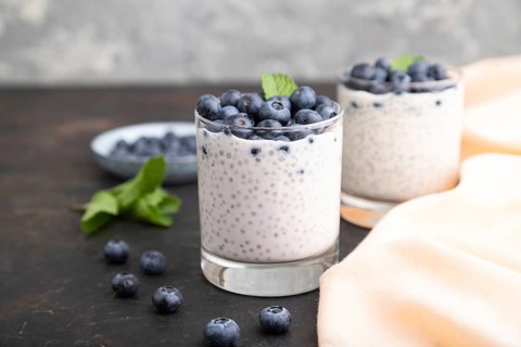 Yogurt with blueberry and chia in glass on black concrete background and orange linen textile. Side