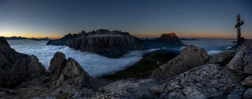 Summit cross of the large Cirrspitze with sunrise over a sea of fog and Dolomite peaks in the