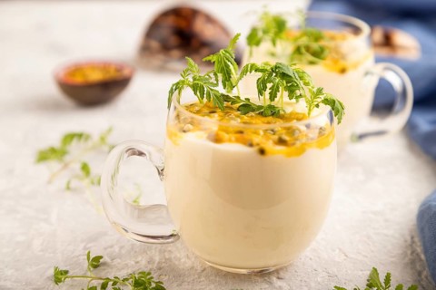 Yogurt with passionfruit and marigold microgreen in glass on gray concrete background with blue