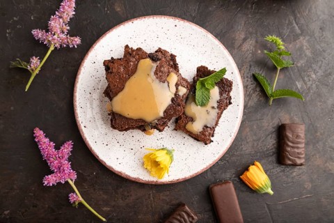 Chocolate brownie with caramel sauce with a cup of coffee on black concrete background. top view,