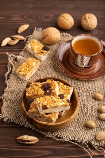 Traditional candy nougat with nuts and sesame with cup of green tea on brown wooden background and