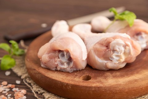 Raw chicken legs with herbs and spices on a wooden cutting board on a brown wooden background and