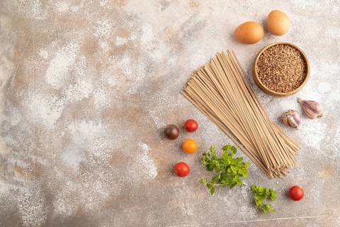 Japanese buckwheat soba noodles with tomato, eggs, spices, herbs on brown concrete background. Top