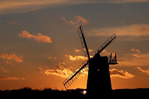 Windmill silhouetted at sunset with a red sky and clouds and a skein or flock of Pink-footed geese