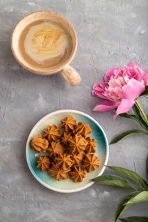 Homemade soft caramel fudge candies on blue plate and cup of coffee on gray concrete background,