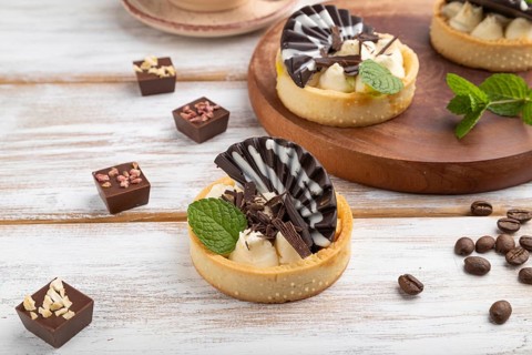 Sweet tartlets with chocolate and cheese cream with cup of coffee on a white wooden background and