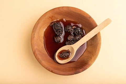 Pine cone jam in wooden bowl on orange pastel background. Top view, flat lay, close up