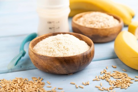 Powdered milk and oatmeal, banana baby food mix, infant formula, pacifier, bottle, spoon on blue