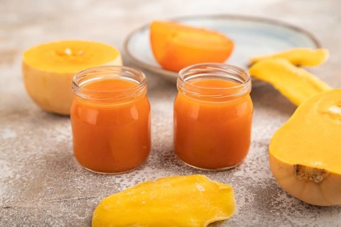 Baby puree with fruits mix, pumpkin, persimmon, mango infant formula in glass jar on brown concrete
