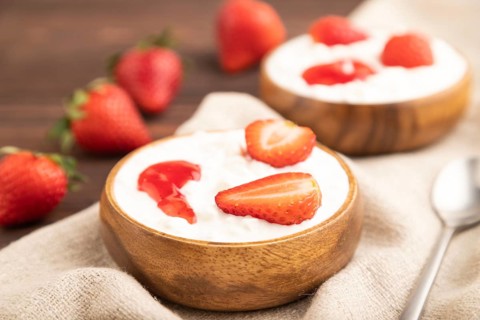 Grained cottage cheese with strawberry jam on brown wooden background and linen textile. side view,
