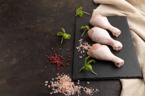 Raw chicken legs with herbs and spices on a black slate cutting board on a black concrete