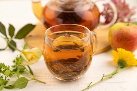 Red tea with herbs in glass teapot on white wooden background. Healthy drink concept. Top view,