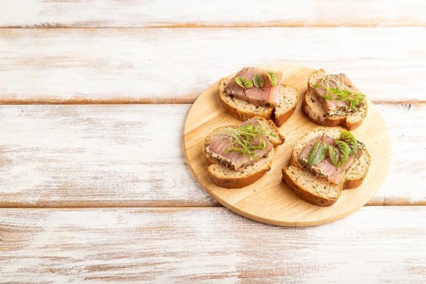 Bread sandwiches with jerky salted meat, sorrel and cilantro microgreen on white wooden background.