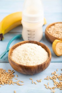 Powdered milk and oatmeal, banana baby food mix, infant formula, pacifier, bottle, spoon on blue