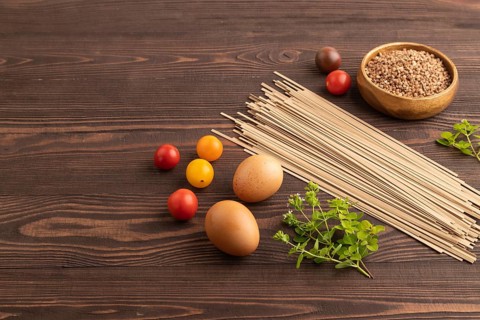 Japanese buckwheat soba noodles with tomato, eggs, spices, herbs on brown wooden background. Side