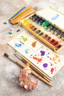Drawing accessories set: brushes, pencils, watercolor on brown concrete background. Side view,