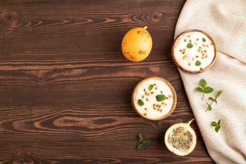 Yoghurt with granadilla and mint in wooden bowl on brown wooden background and linen textile. top
