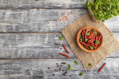 Small smoked sausage with borage microgreen, salt and pepper on gray wooden background and linen