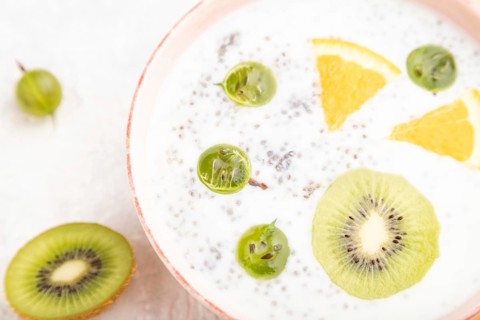Yogurt with kiwi, gooseberry, chia in ceramic bowl on gray concrete background and orange linen
