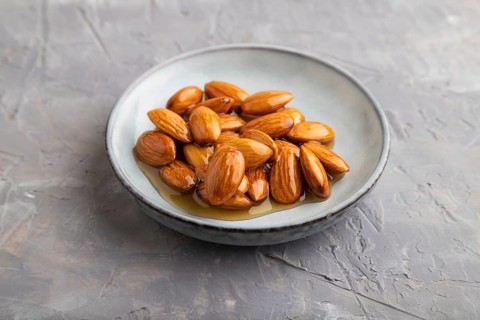 Almonds with honey on gray concrete background. side view, close up