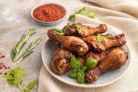 Smoked chicken legs with herbs and spices on a ceramic plate with linen textile on a brown concrete